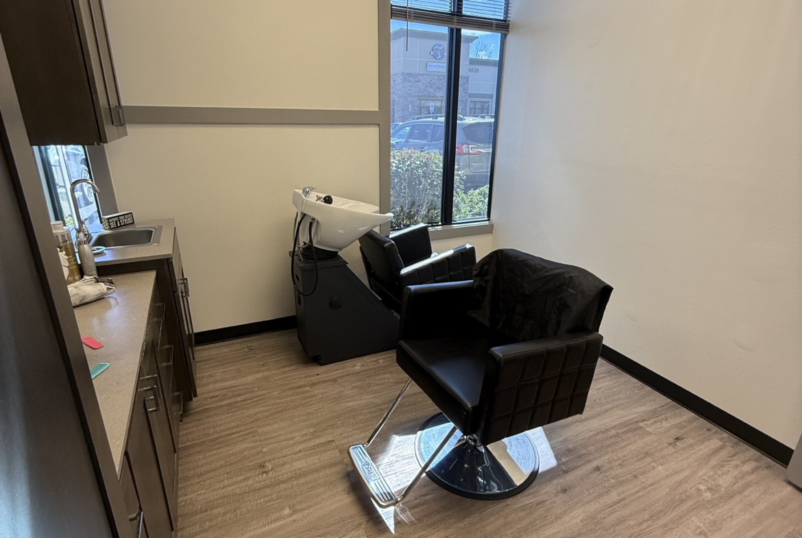 Clean salon station with styling chair, shampoo basin, and large window for natural light.