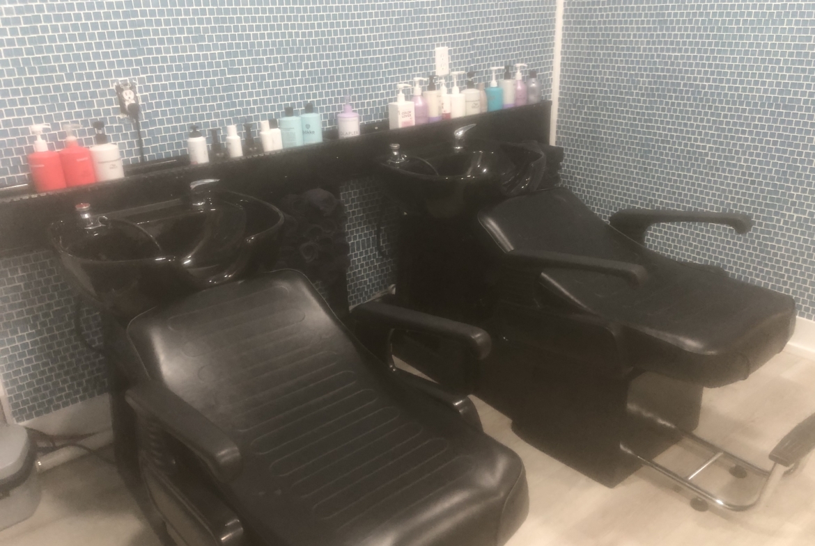 Relaxing salon shampoo stations with black chairs and assorted hair care products.