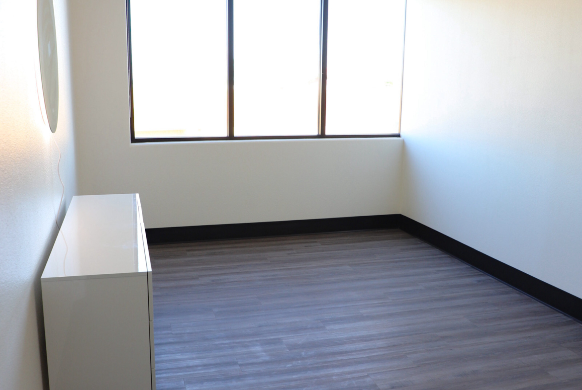 Bright empty room ideal for salon rental with large window and sleek flooring.