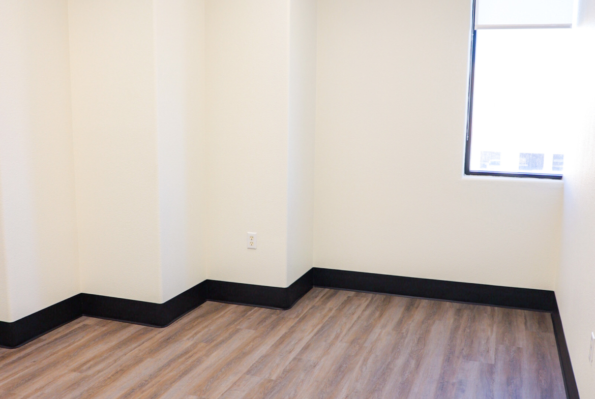 Bright empty studio with hardwood floors and large window, ideal for beauty or hair salon.