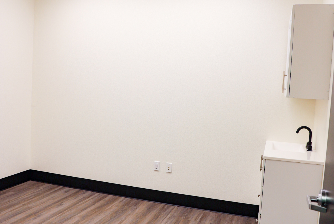 Bright empty salon room with wood flooring and sink, perfect for rent or salon suites.