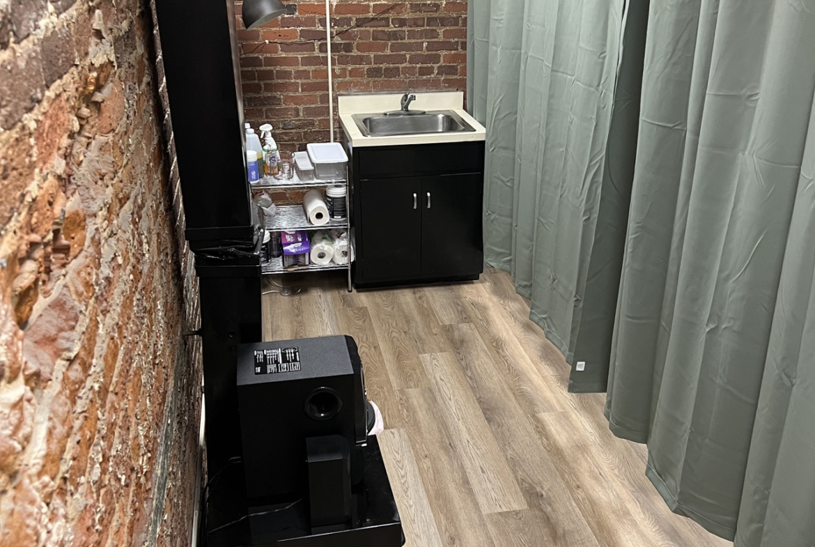 Compact salon workspace with brick walls, sink, and privacy curtains. Perfect for rent or leasing studio space.