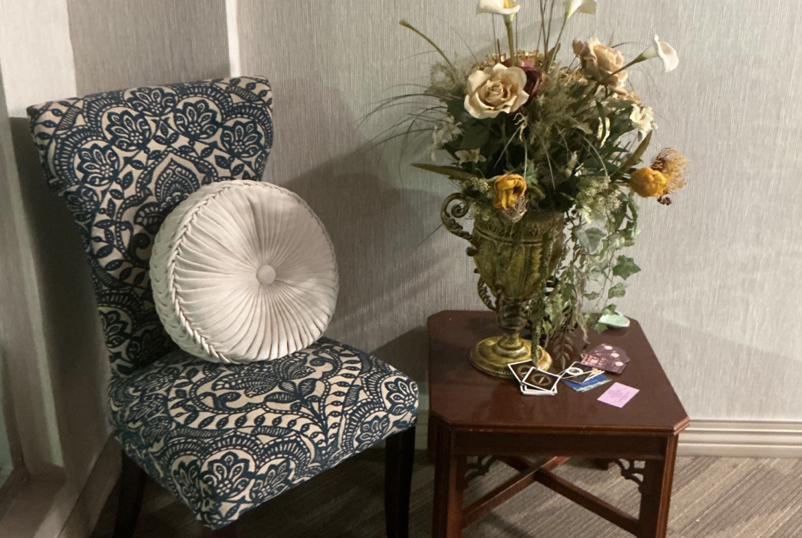 Decorative chair with floral cushion beside a table with flower arrangement in salon.