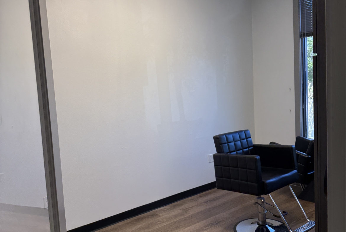Empty hair salon room with styling chairs, chandelier, and natural light, perfect for salon leasing.