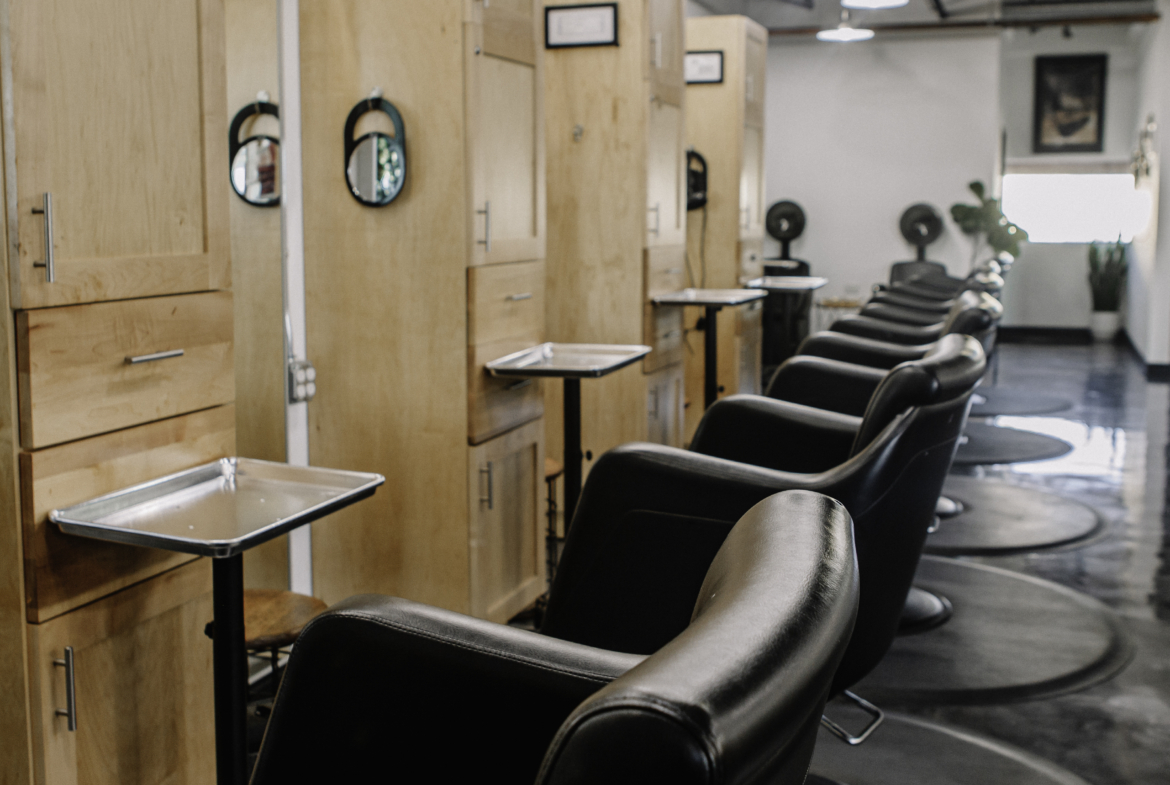 Bright modern hair salon interior with black styling chairs, wooden stations, and overhead lighting.