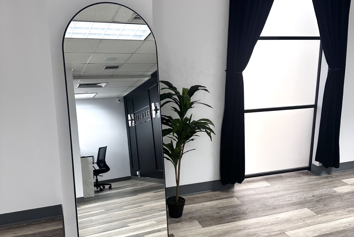 Bright, spacious salon with large mirror, black curtains, and wooden flooring for beauty professionals.