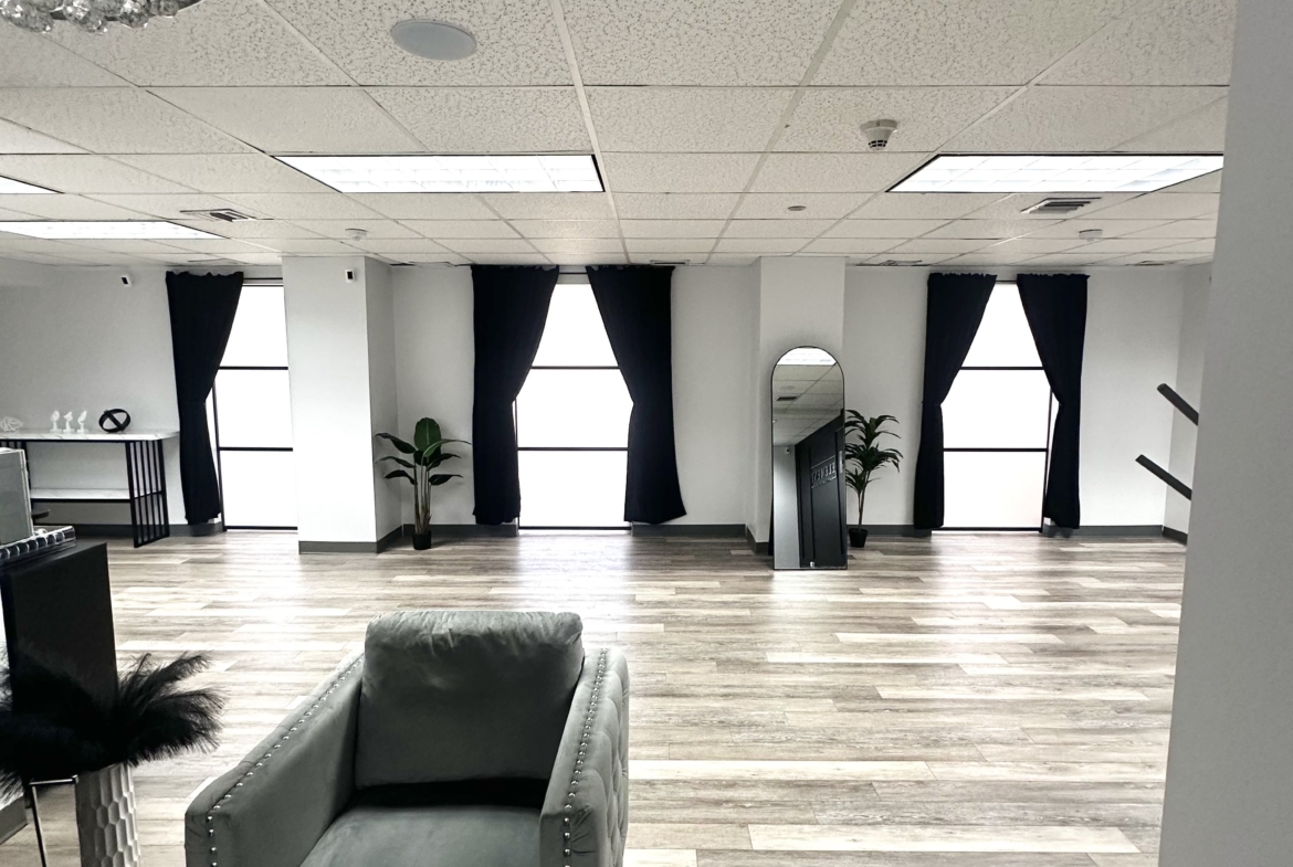 Bright salon rental space with large windows, black curtains, and contemporary decor, ideal for beauty professionals.