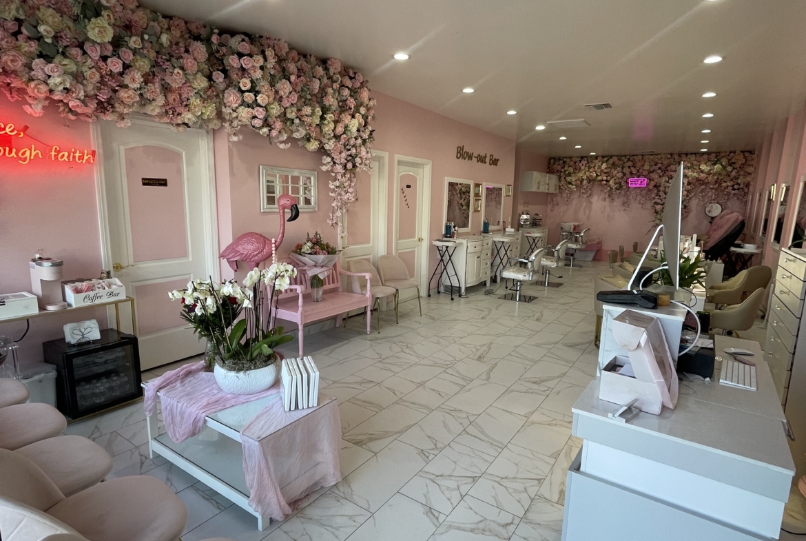A stylish, feminine salon space featuring pink flowers, cozy chairs, and elegant decor.