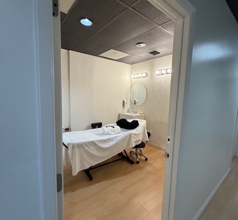 A professional salon room with treatment bed, mirror, and lighting for beauty services.