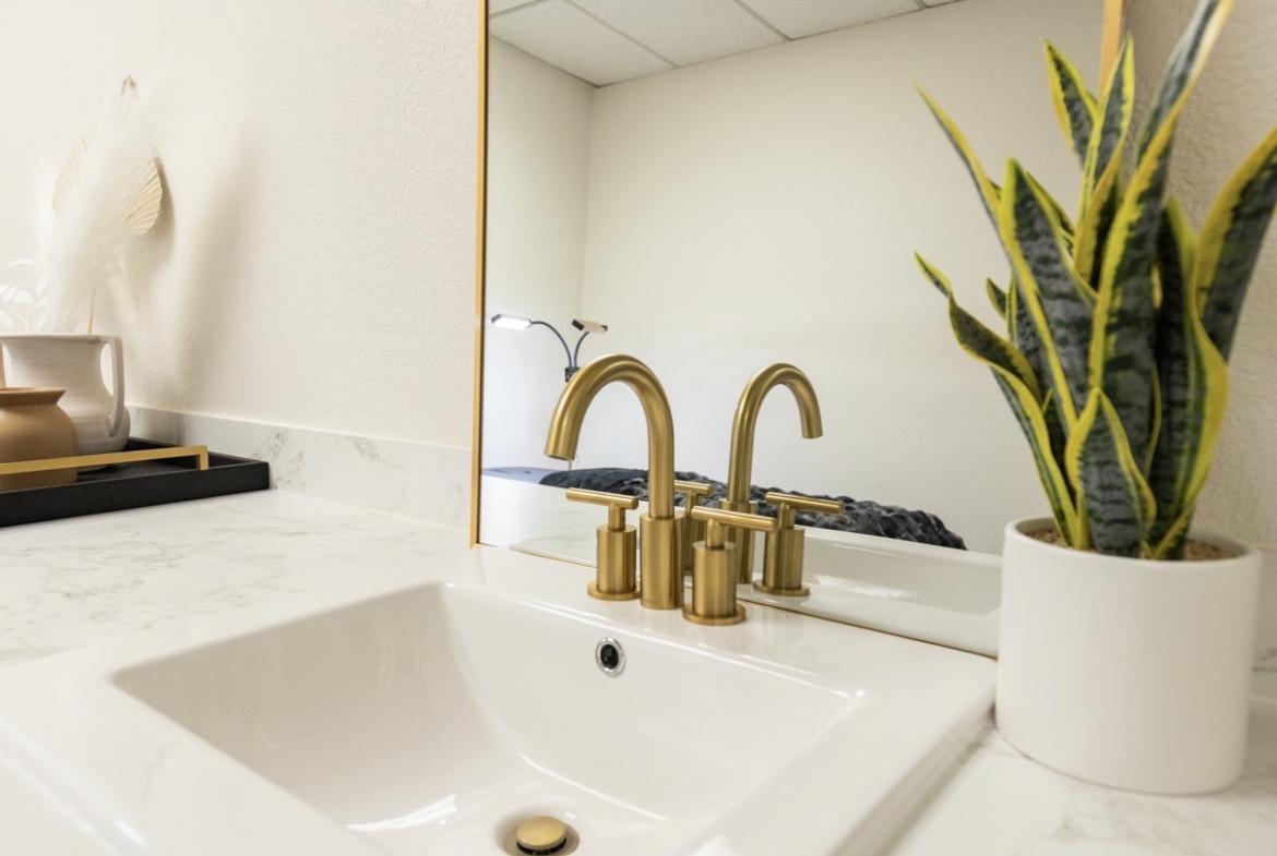 Clean modern bathroom sink with gold fixtures and a mirror.