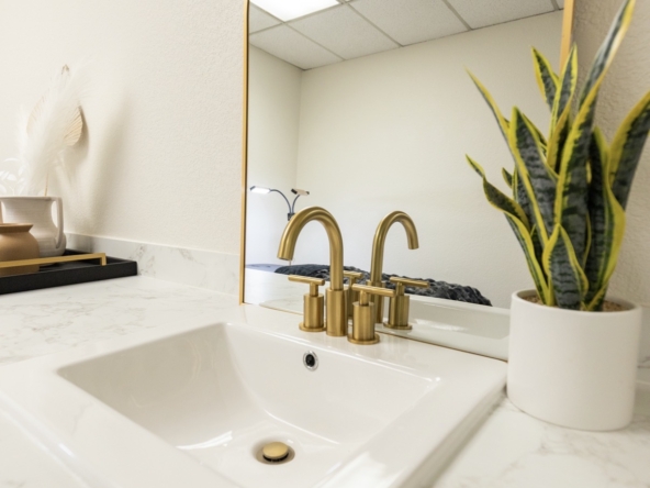 Clean modern bathroom sink with gold fixtures and a mirror.