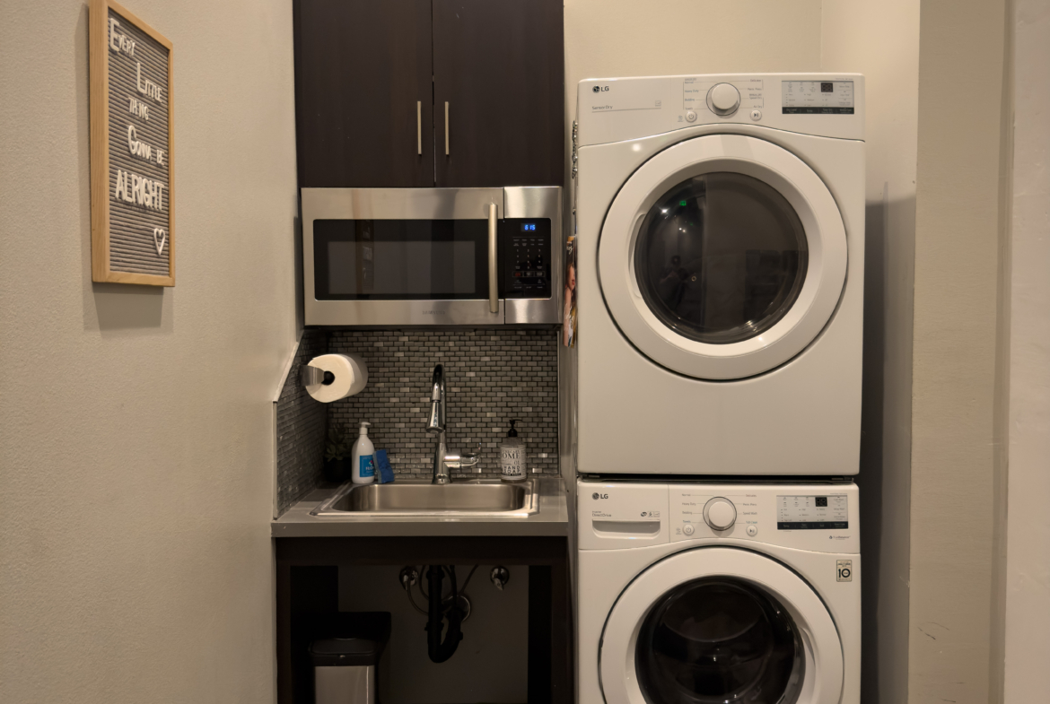 Stacked washer and dryer with a small laundry sink and microwave in a salon or spa setting.