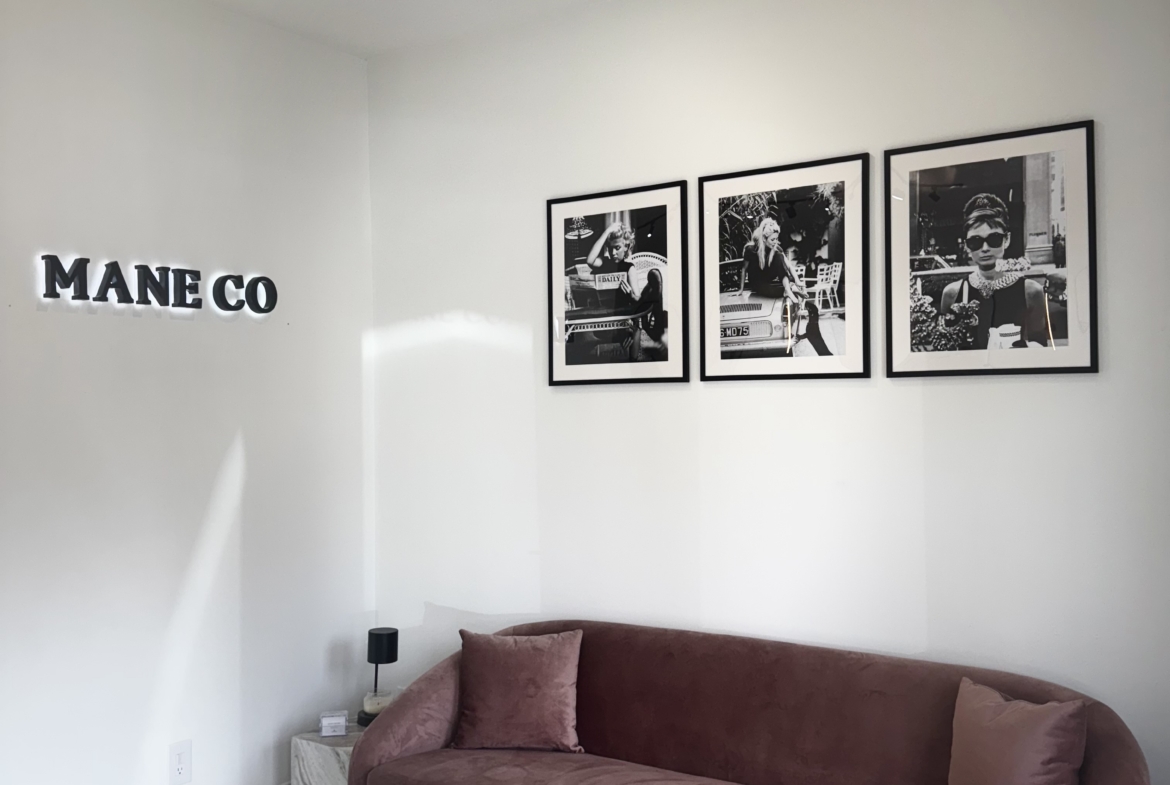 Stylish waiting area with pink velvet sofa, black and white photography art, and salon branding.