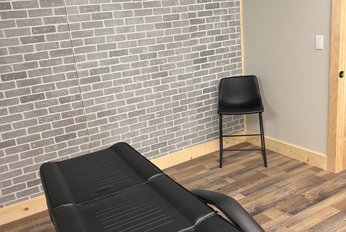 Modern salon treatment room with brick wall and black reclining chair, ideal for hair or beauty services.