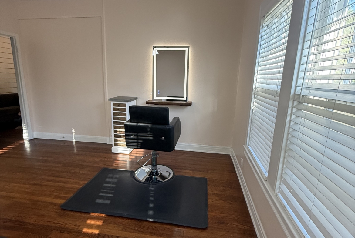 Stylish salon interior featuring a comfortable styling station, bright natural lighting, and hardwood floors.