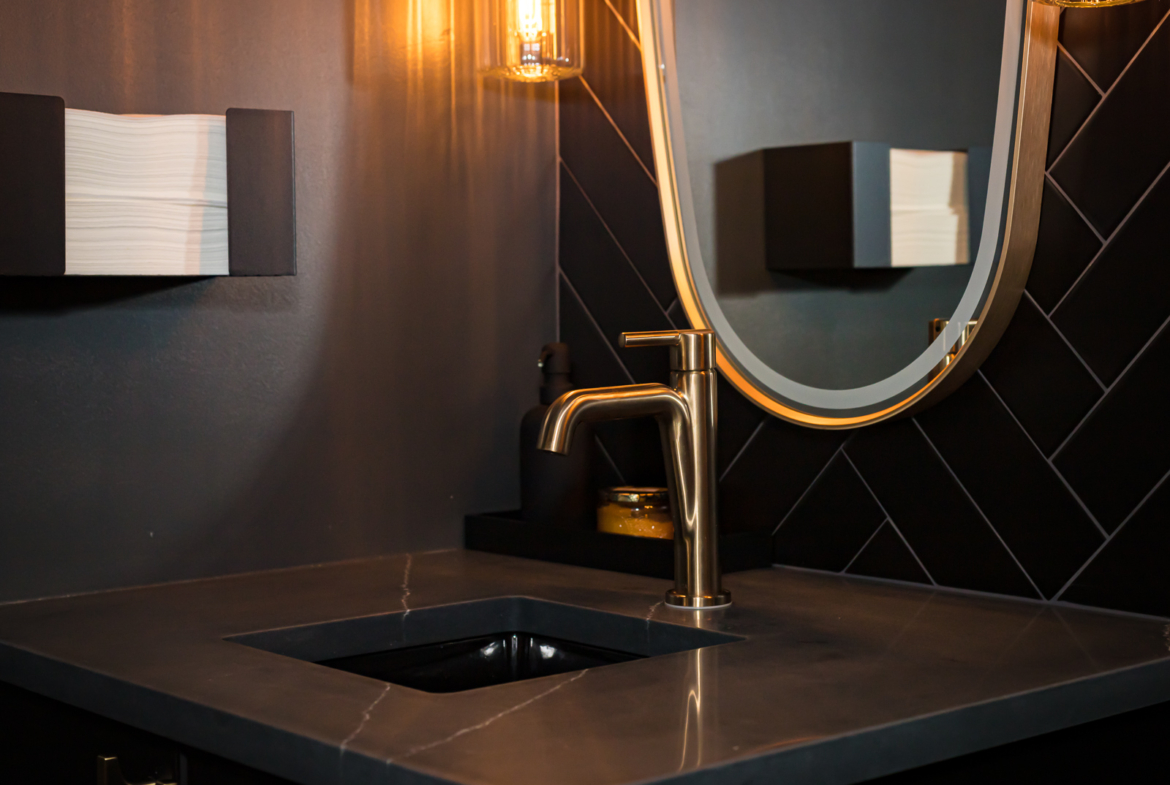 Luxury salon bathroom sink with modern black countertop, gold faucet, and stylish mirror.