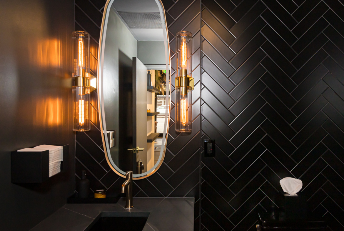Stylish bathroom featuring black herringbone tiles, vintage lighting, and a sleek vanity mirror at Salon Renter.