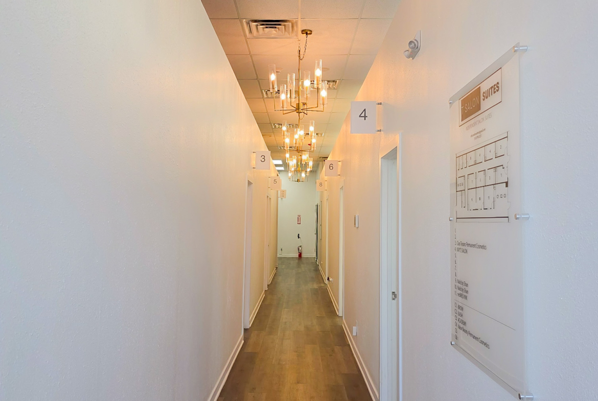 Bright hallway with chandeliers, numbered salon suites, clean walls, and wooden flooring.