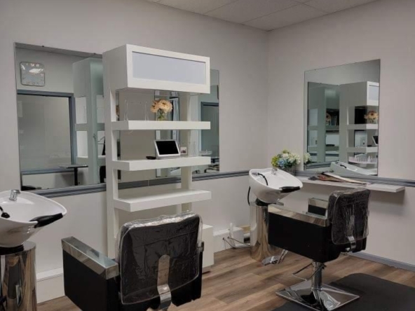 A contemporary salon station with black chairs, mirrors, and washing sinks for hair treatments.
