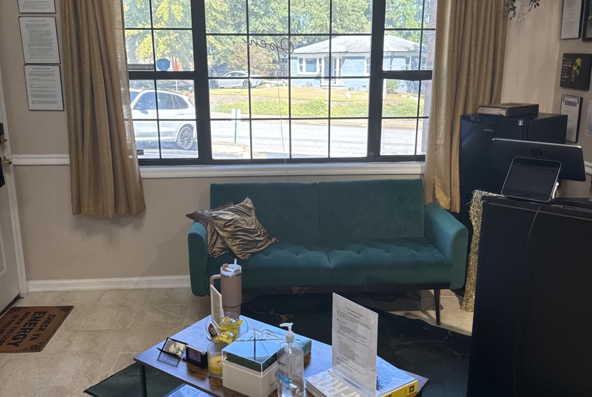 Interior of salon waiting area with green sofa, wall decor, and a large window overlooking the street.