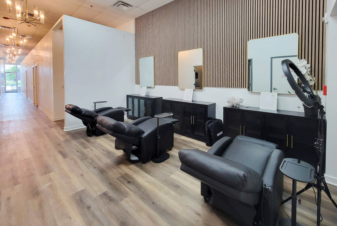 Stylish hair salon styling area with black reclining chairs, mirrors, and wooden decor.