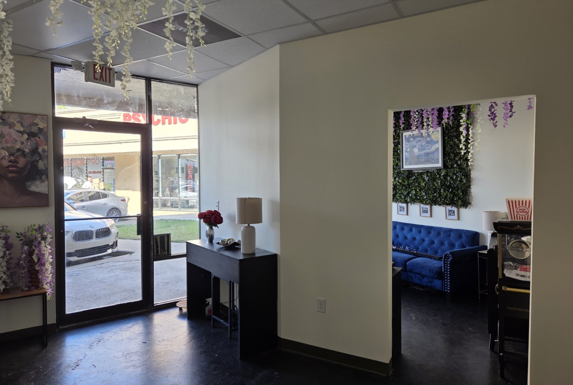 Bright salon entrance featuring large glass door and exterior view of parked cars.