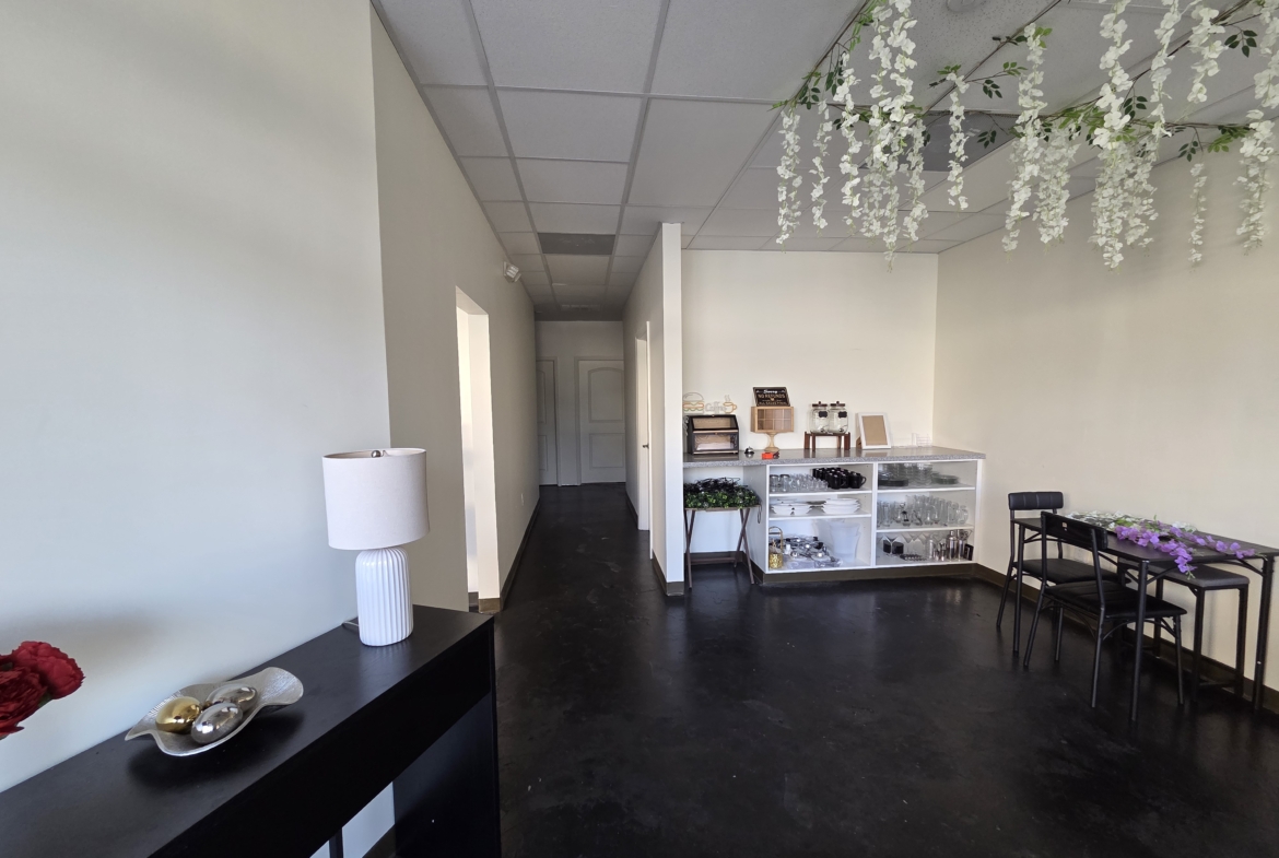 Bright salon reception with white walls, black furniture, decorative flowers, and organized shelving units.
