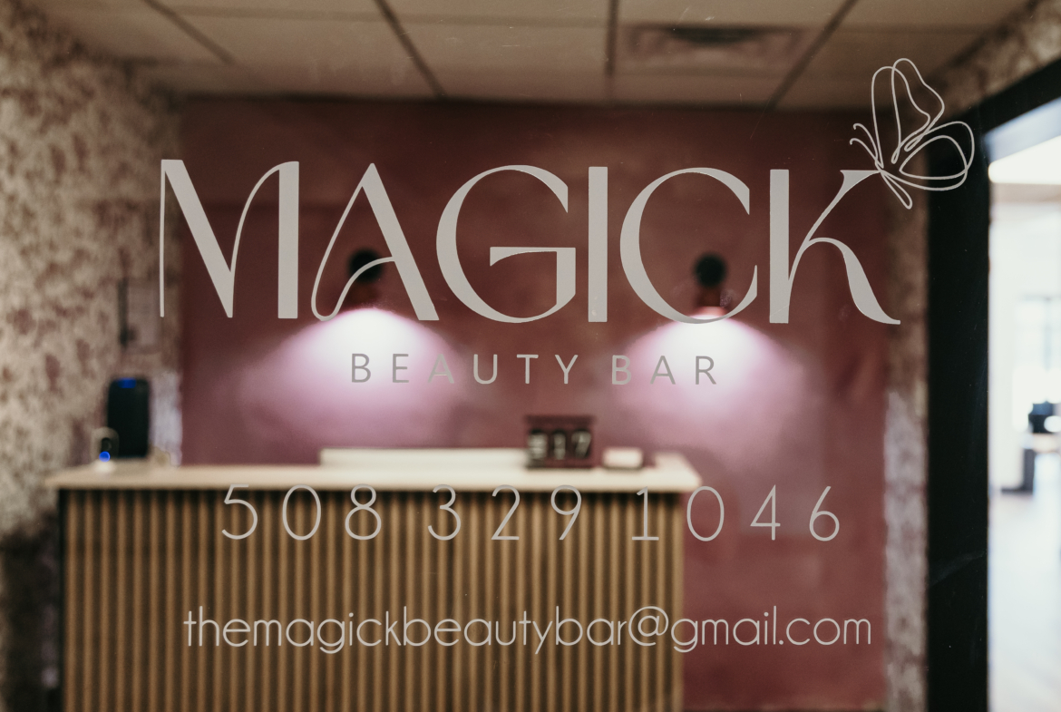 Close-up of "Magic Beauty Bar" logo and contact info on glass door at a trendy hair and beauty salon.