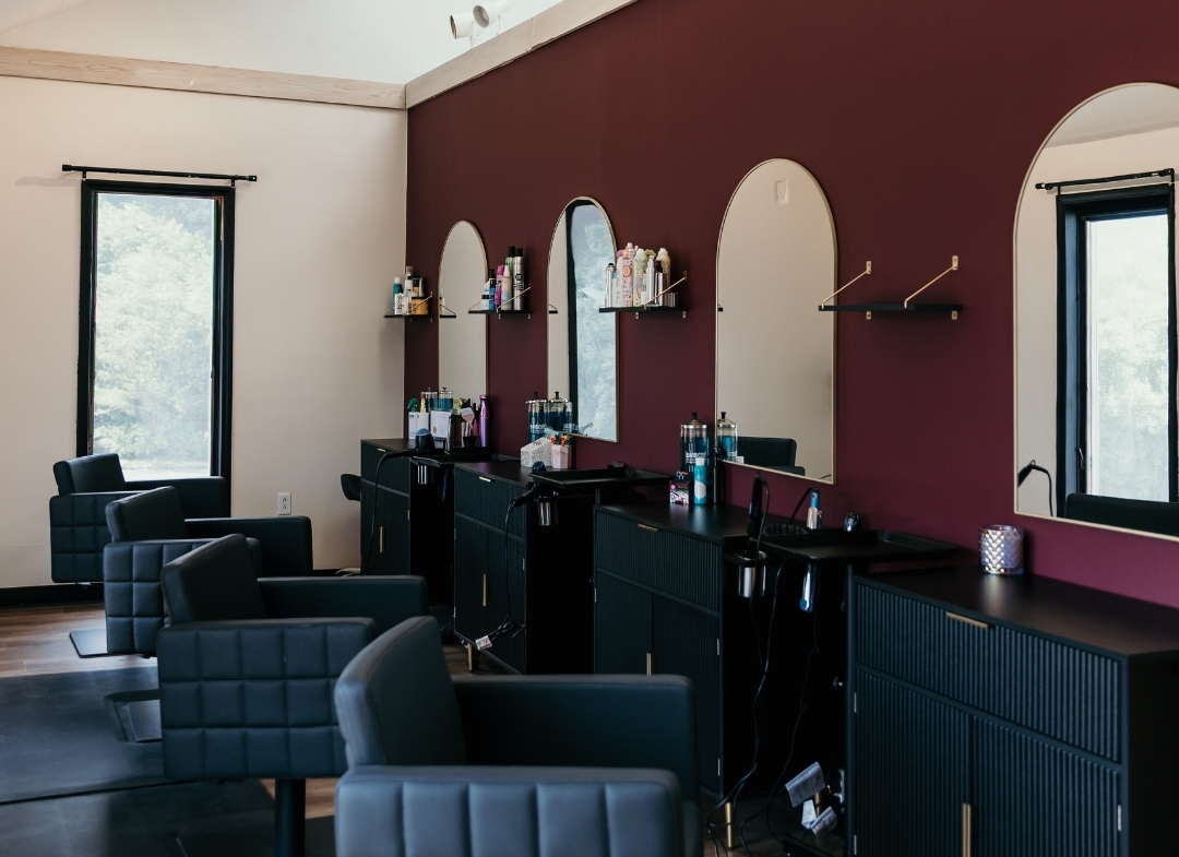 Modern hair salon with black styling chairs, mirrors, and professional hair products.
