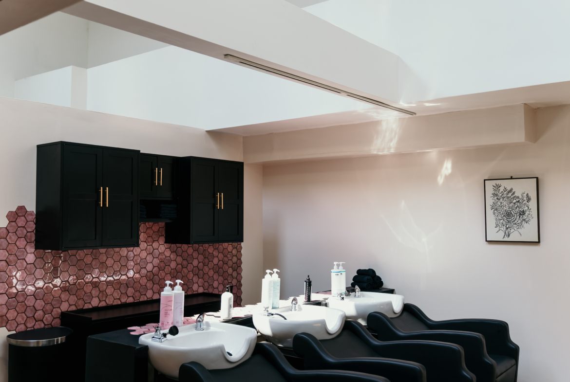 Relaxing salon hair washing area with black chairs, pink accents, and wooden floors.