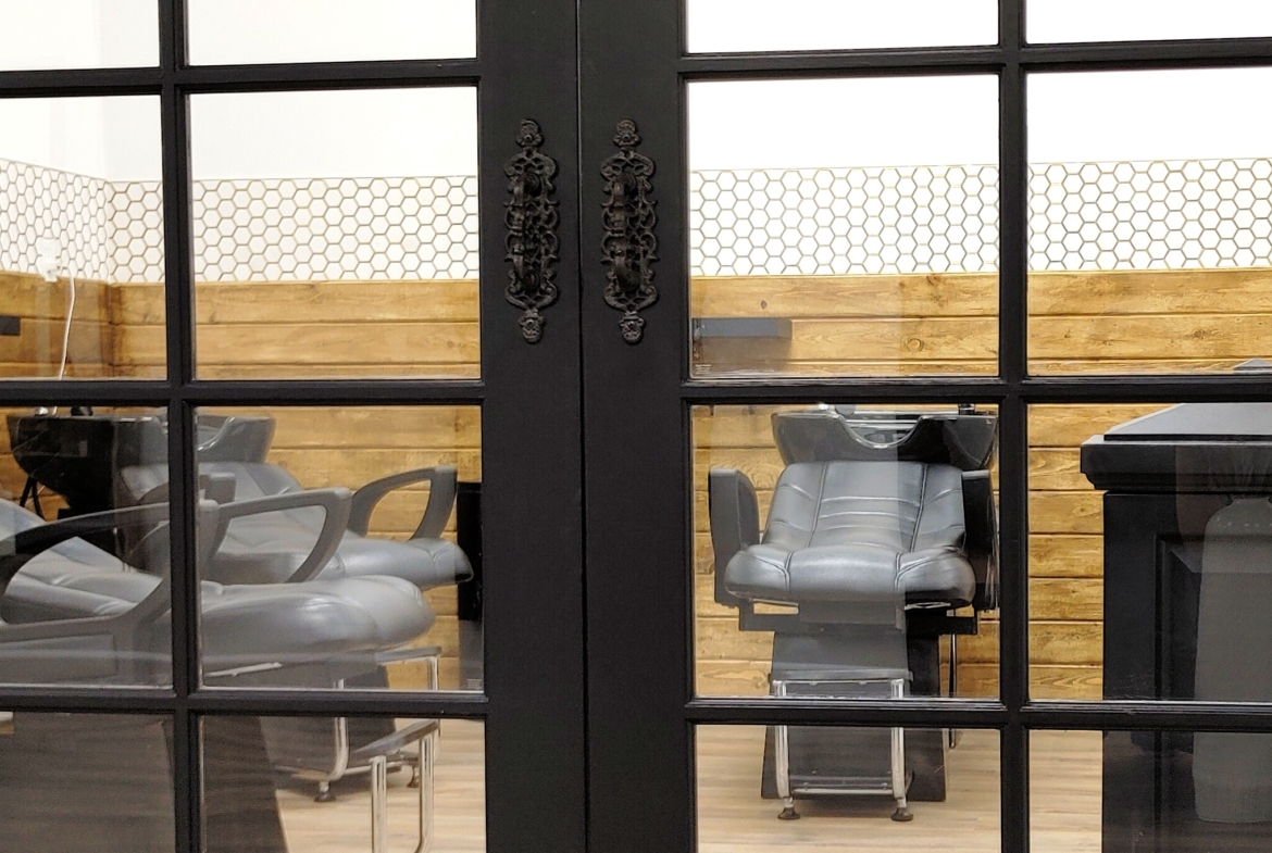 Salon interior view through glass door, featuring styling chairs and wooden accents.