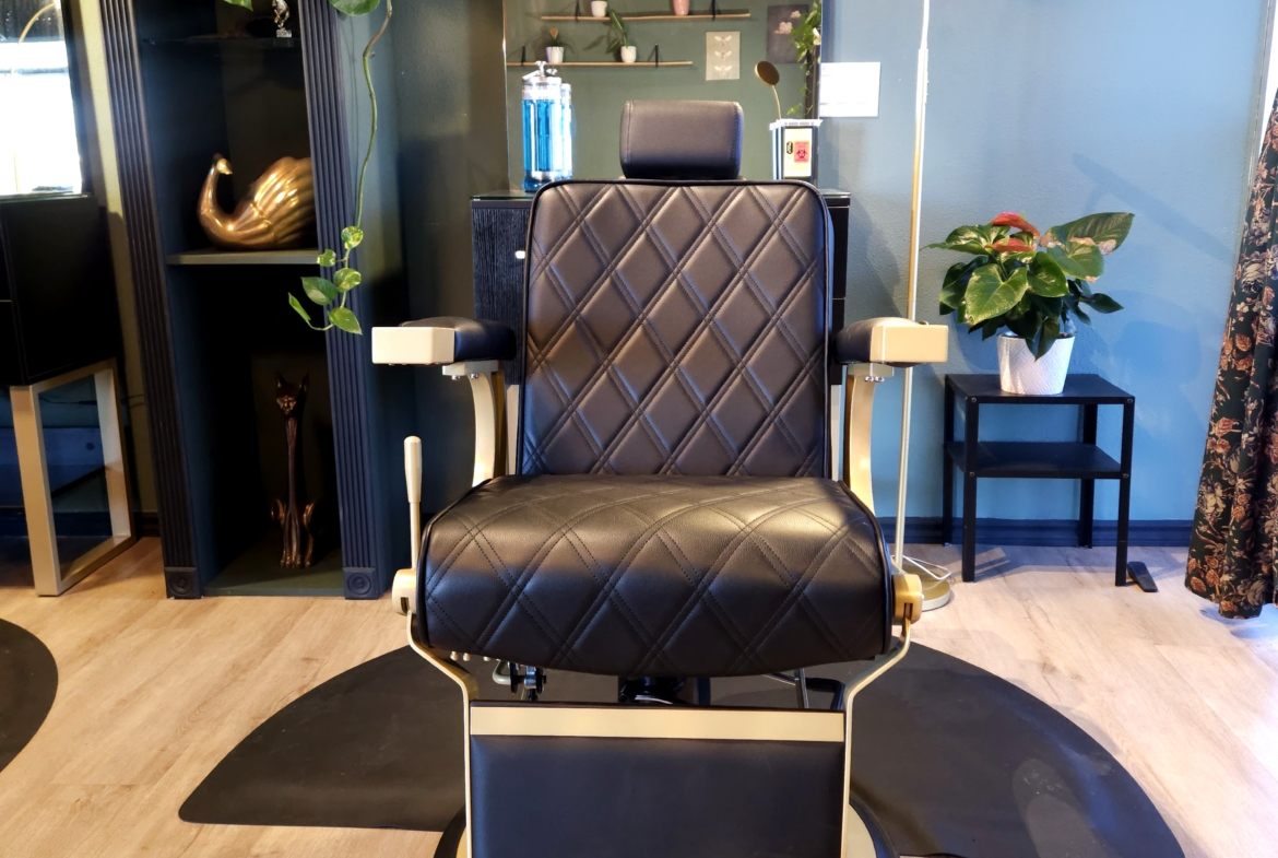 Stylish salon barber chair with black quilted upholstery, surrounded by plants and trendy decor.