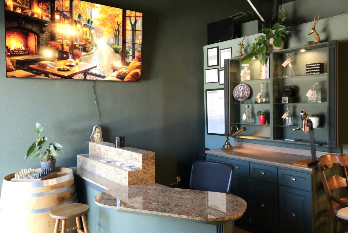 A stylish salon reception area with green walls, a TV displaying autumn scenery, and modern decor including plants and artwork for a welcoming atmosphere.