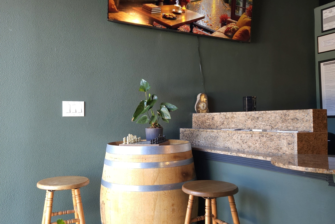 Relaxing salon interior with green accent wall, plant, wooden stools, and decorative barrel.