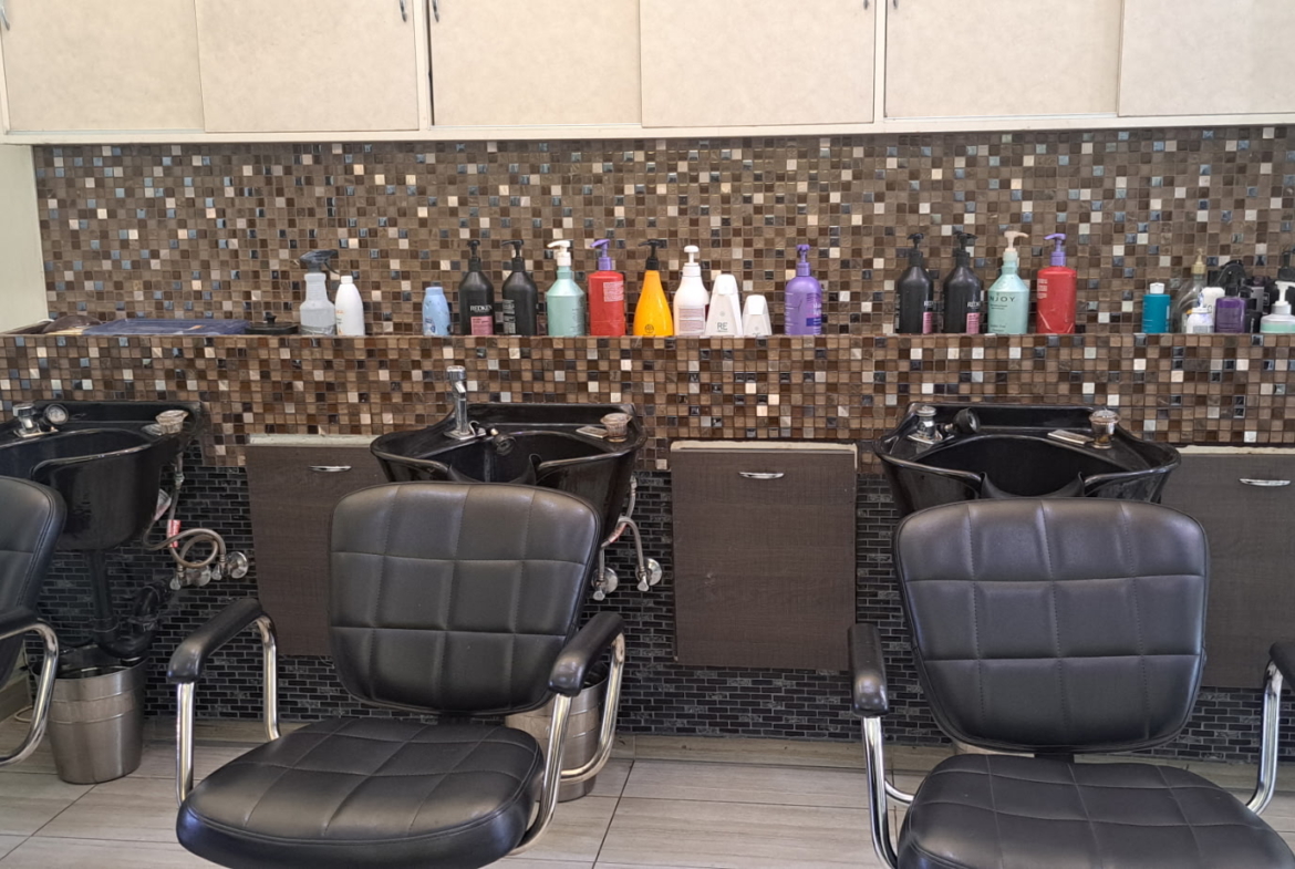 Clean salon shampoo station with black wash bowls, chairs, and hair product bottles.