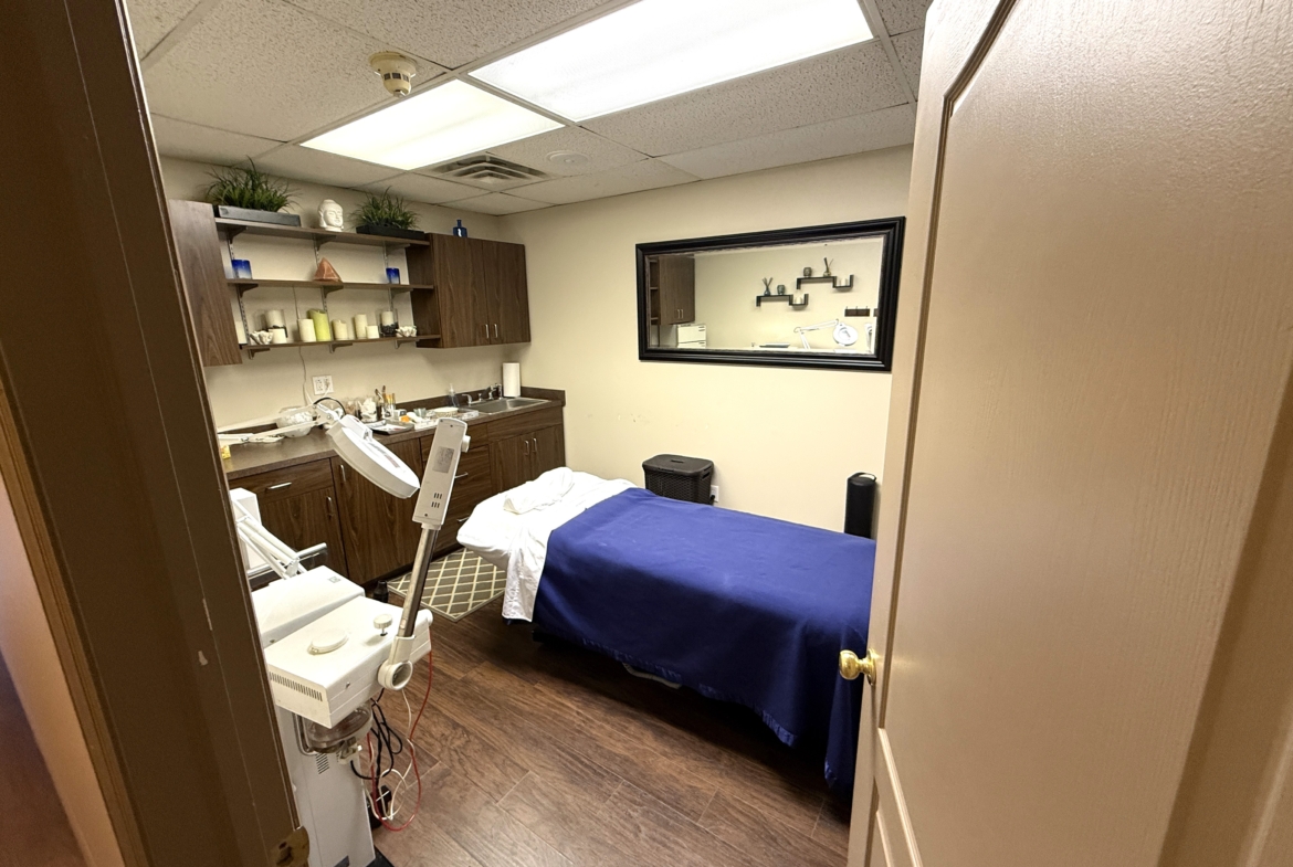 Comfortable salon rental room with massage bed, shelves, and relaxing ambiance.