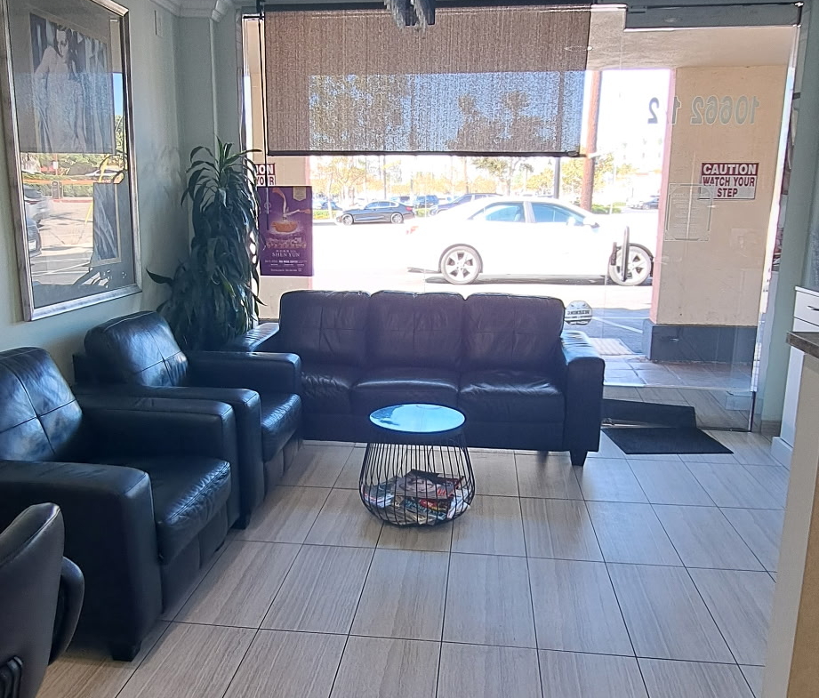 Comfortable salon waiting area with black leather couches and large windows.