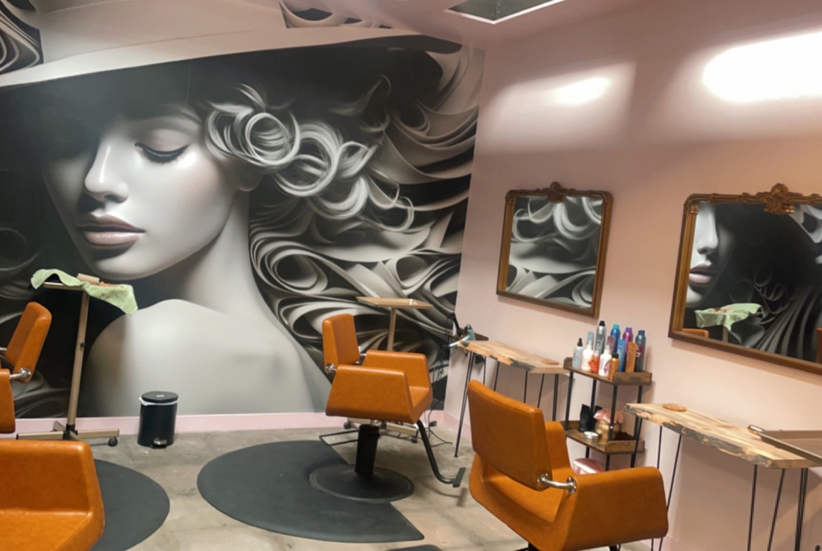 Stylish salon space featuring hair stations, mirrors, chairs, and vibrant wall art for hair and beauty services.