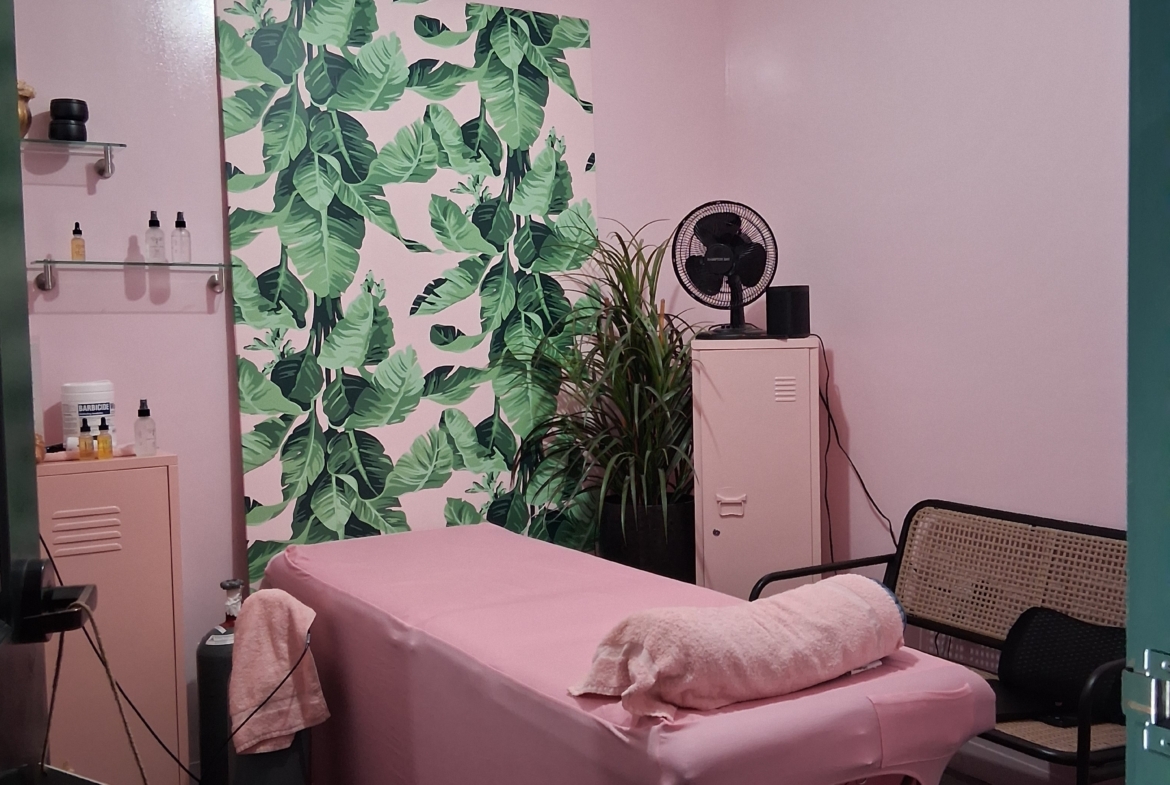 Stylish salon treatment room with pink walls, tropical leaf wall art, and relaxing ambiance. Perfect space for beauty and wellness services.