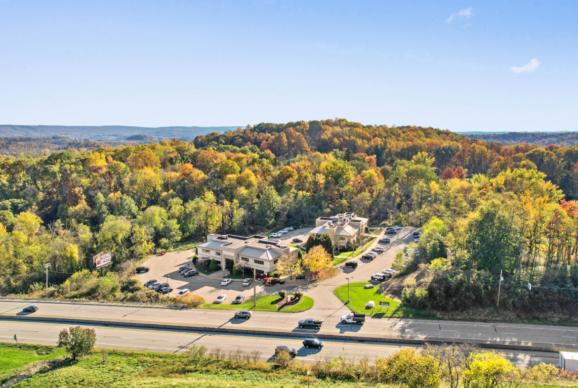 Aerial view of a salon rental building surrounded by colorful autumn trees, near a highway, ideal for salon professionals seeking rental space.