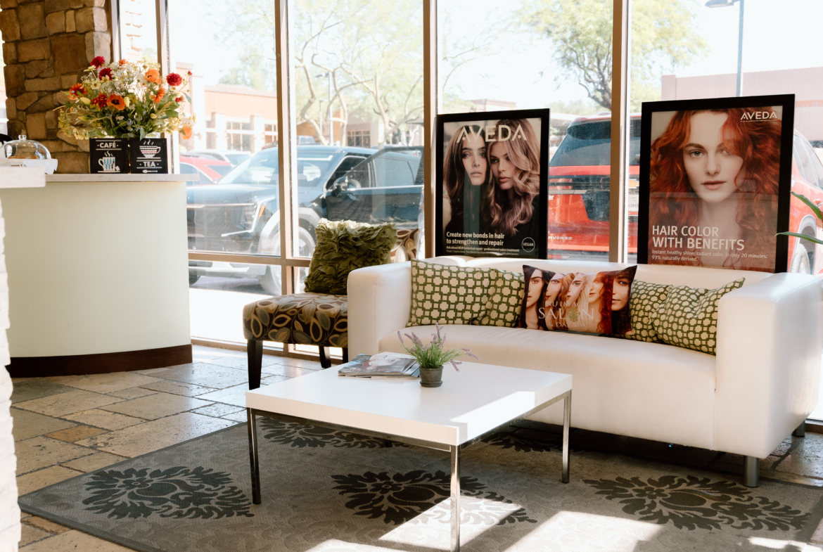 Bright salon lounge with hair advertisement posters, large windows, and inviting seating area.