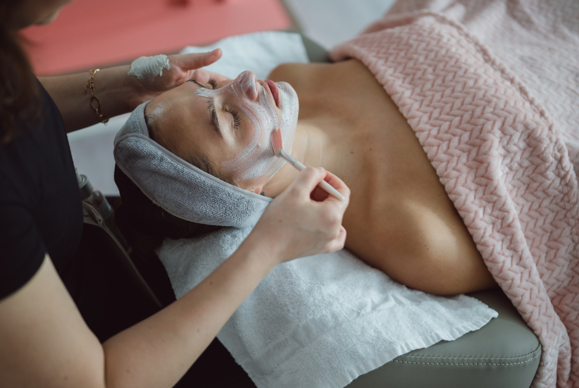 Facialist applying face mask to woman receiving skincare treatment at salon.