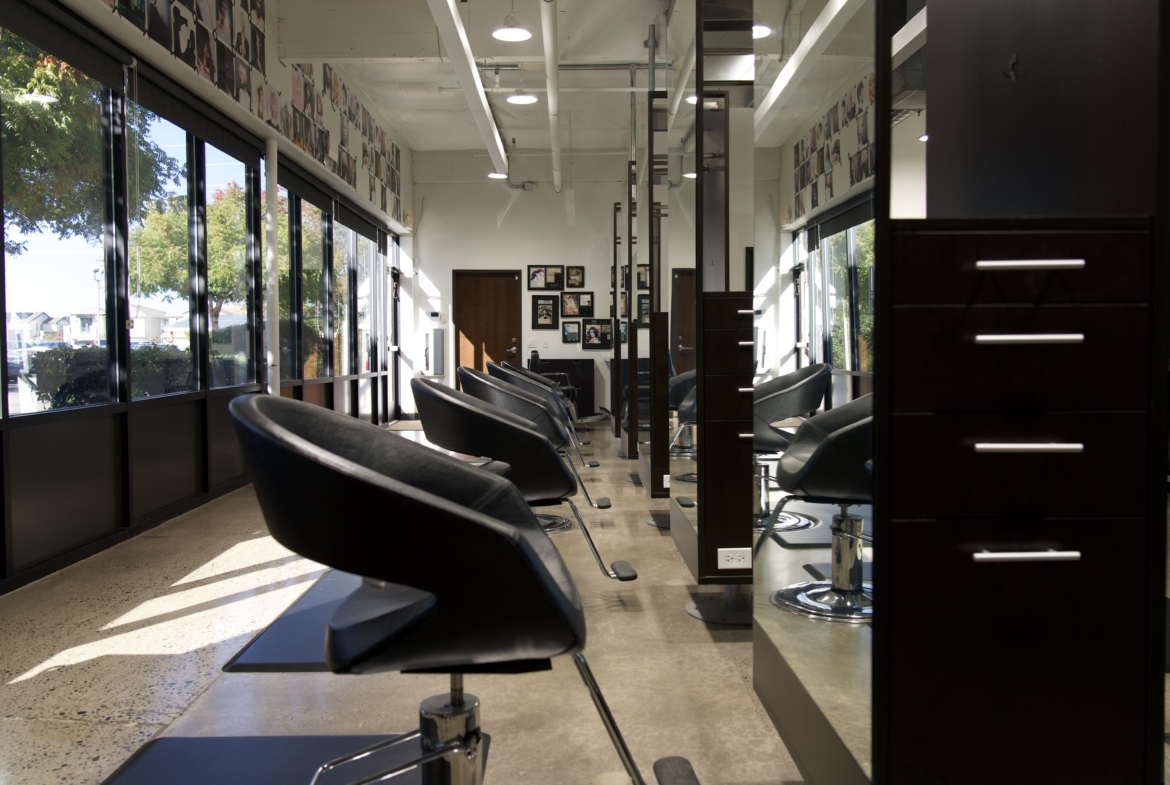 Picture of a stylish, well-lit salon interior featuring sleek black chairs, large windows, and organized stations for hair styling services.
