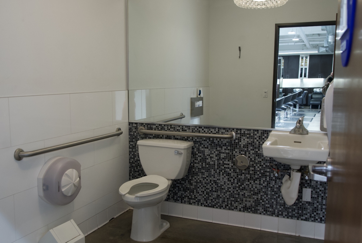 Clean, accessible salon restroom with mirror, toilet, sink, and safety features.