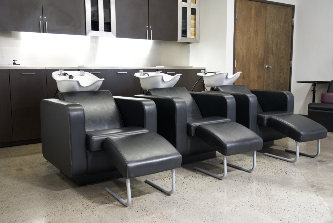 Black leather hair salon chairs with wash basins and modern styling at Salon Renter.