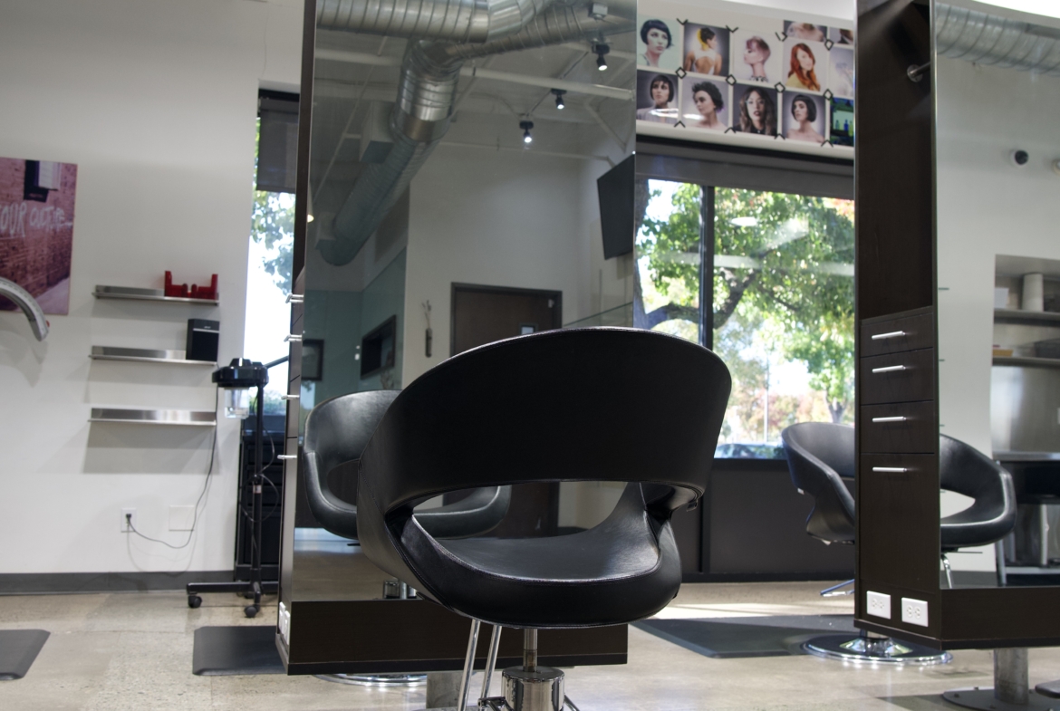 High-resolution image of a contemporary salon station with black styling chair and large mirror, perfect for hair cutting and styling.