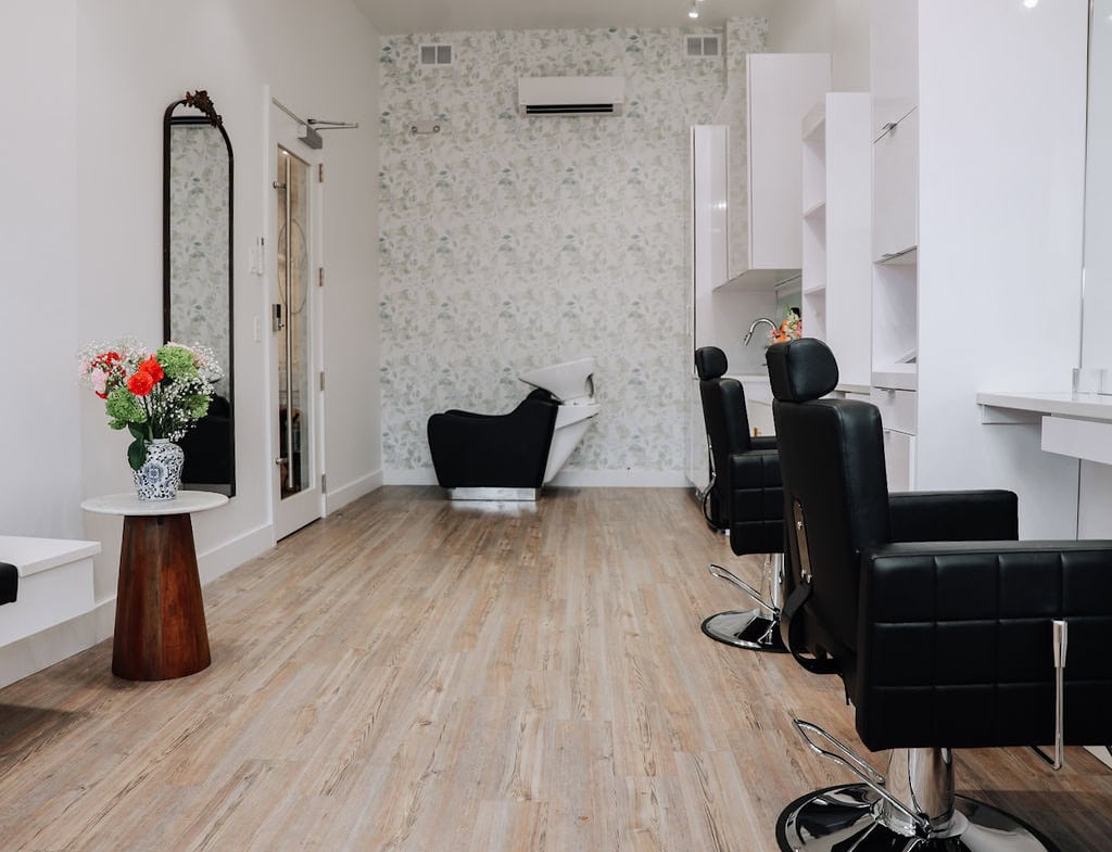 Bright salon with black styling chairs, white cabinets, and a floral accent wall for hair and beauty services.