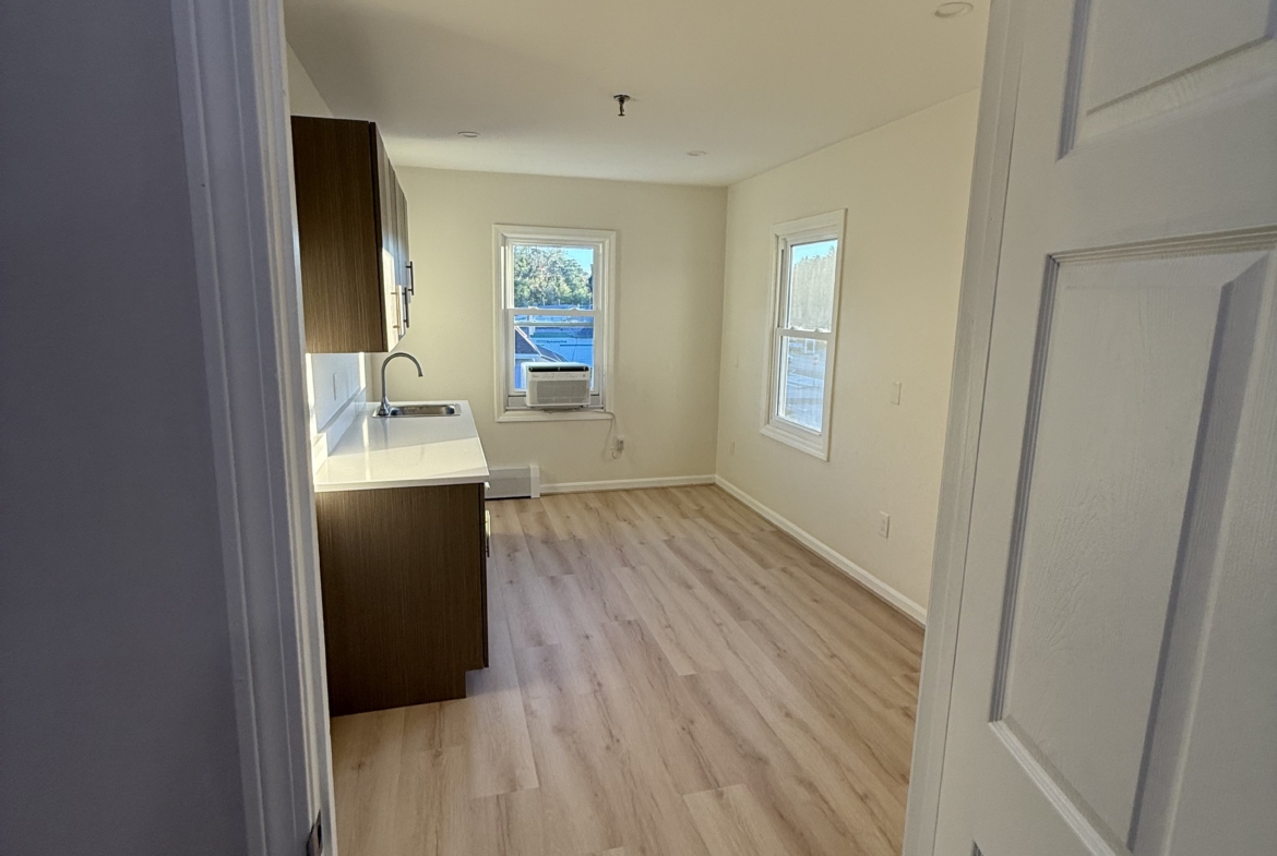 Bright, empty salon rental space with windows and hardwood floors.