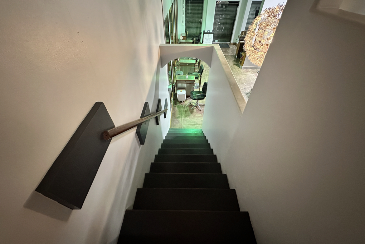 A clean, contemporary salon staircase leading to a stylish beauty studio with vibrant lighting.