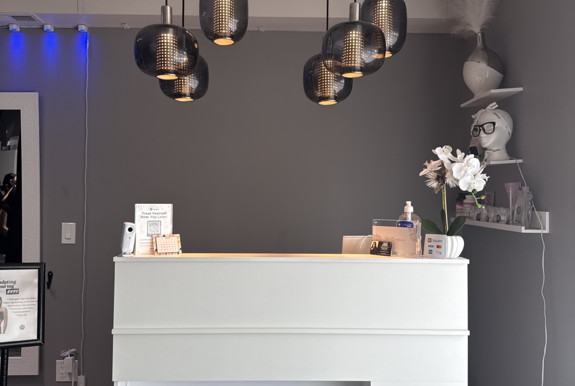 Elegant salon reception area with white counter, modern pendant lights, and chic decor.